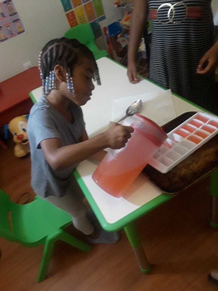 Child pouring liquid from a pitcher into an ice cube tray at a table