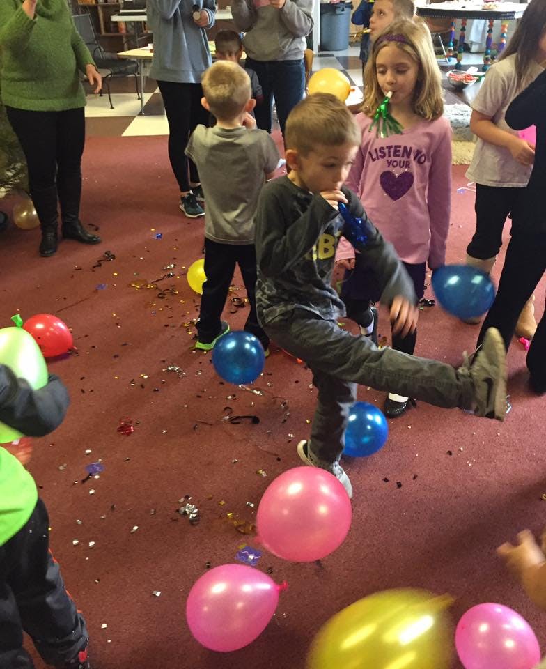 Child kicking a balloon on a confetti-strewn floor with other children