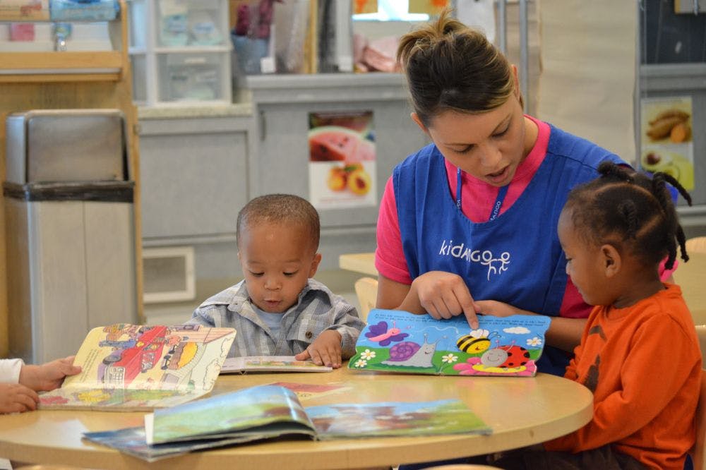 Person reading a book to two children in a classroom