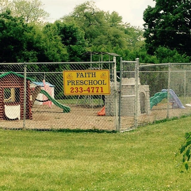 Faith Preschool sign on a chain link fence with playground equipment