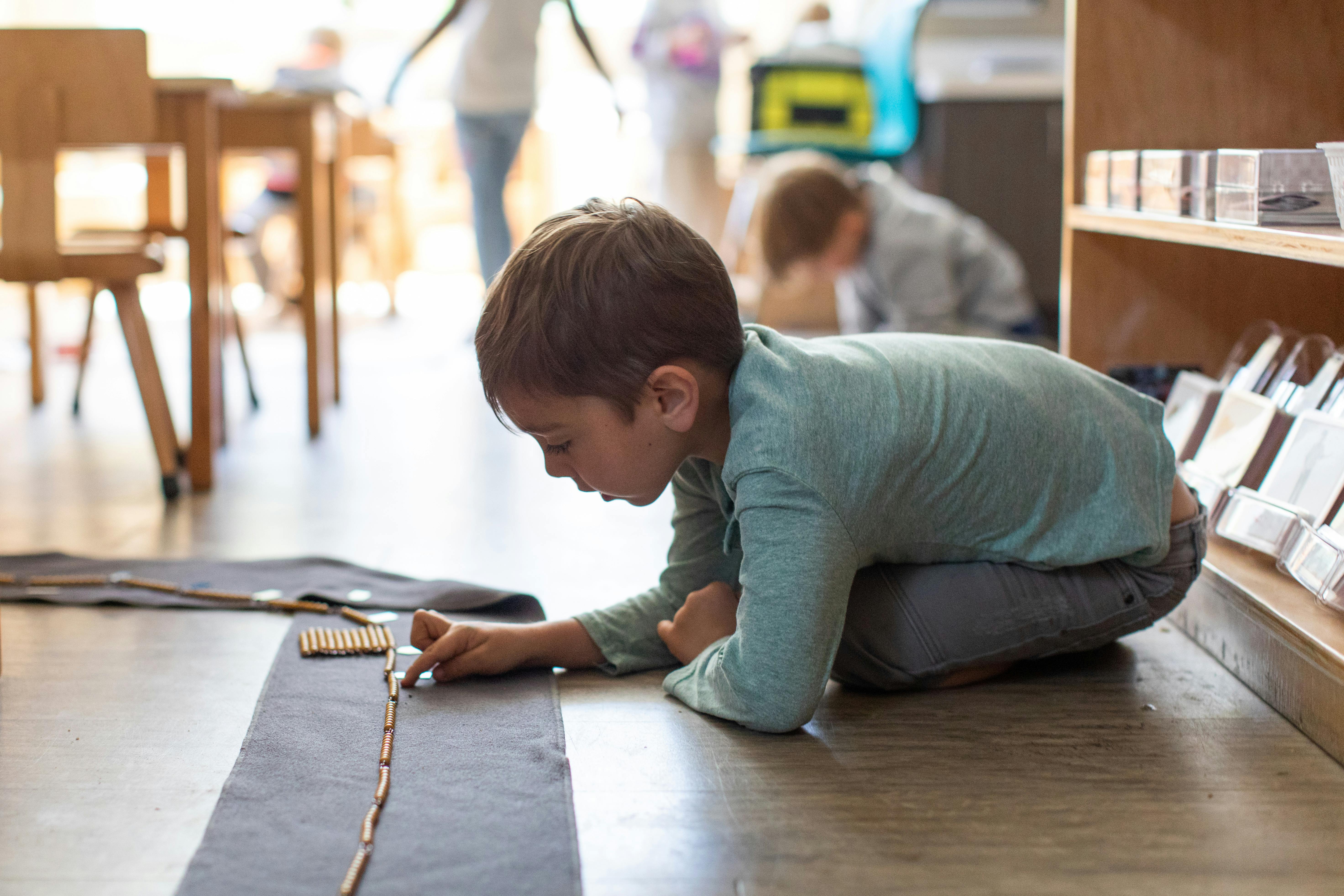 Child kneeling on floor, arranging small objects on a mat
