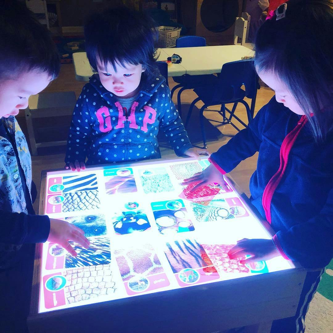 Three children interacting with an illuminated table display