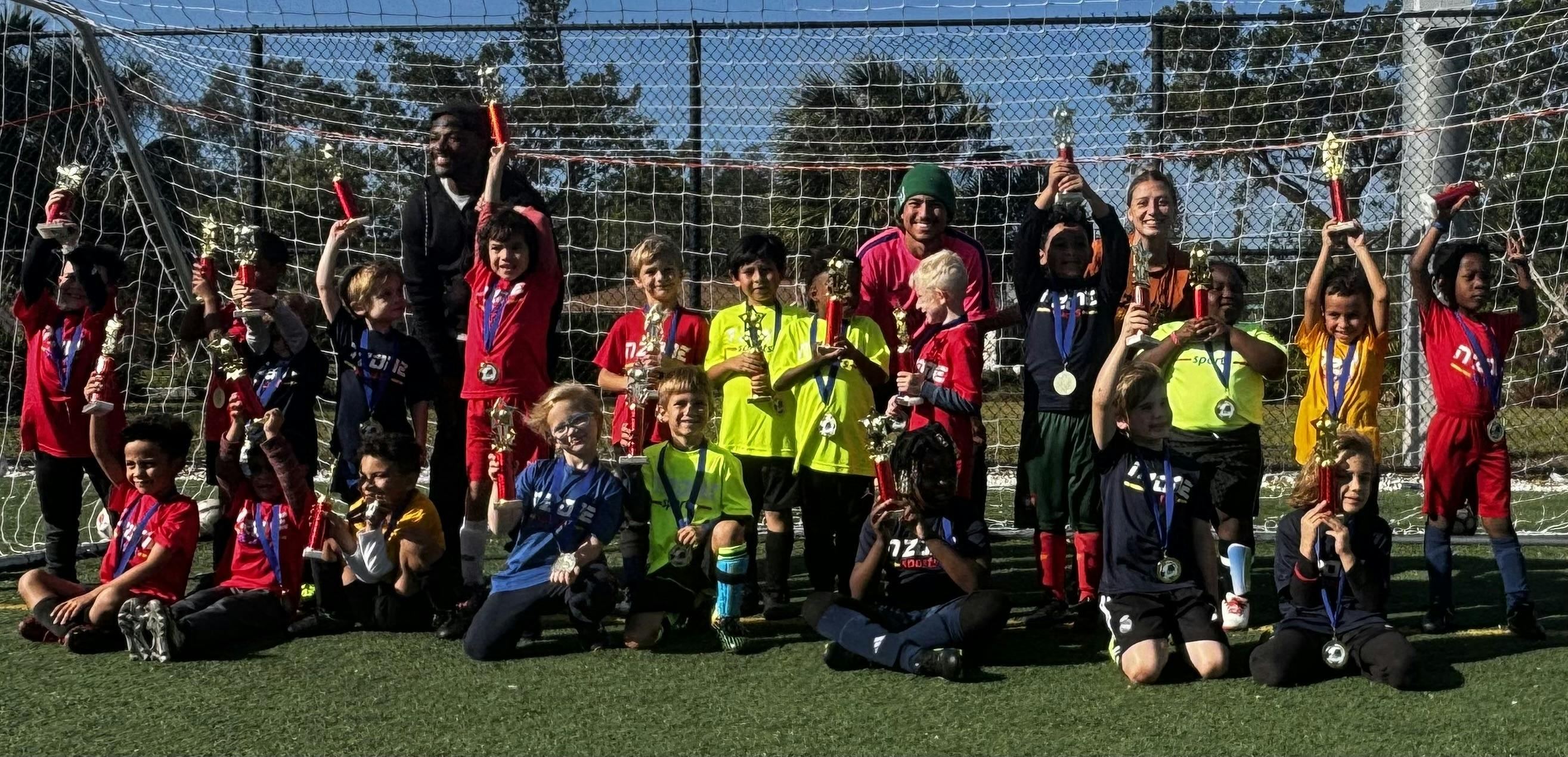 Group of children and adults holding trophies and medals on a soccer field