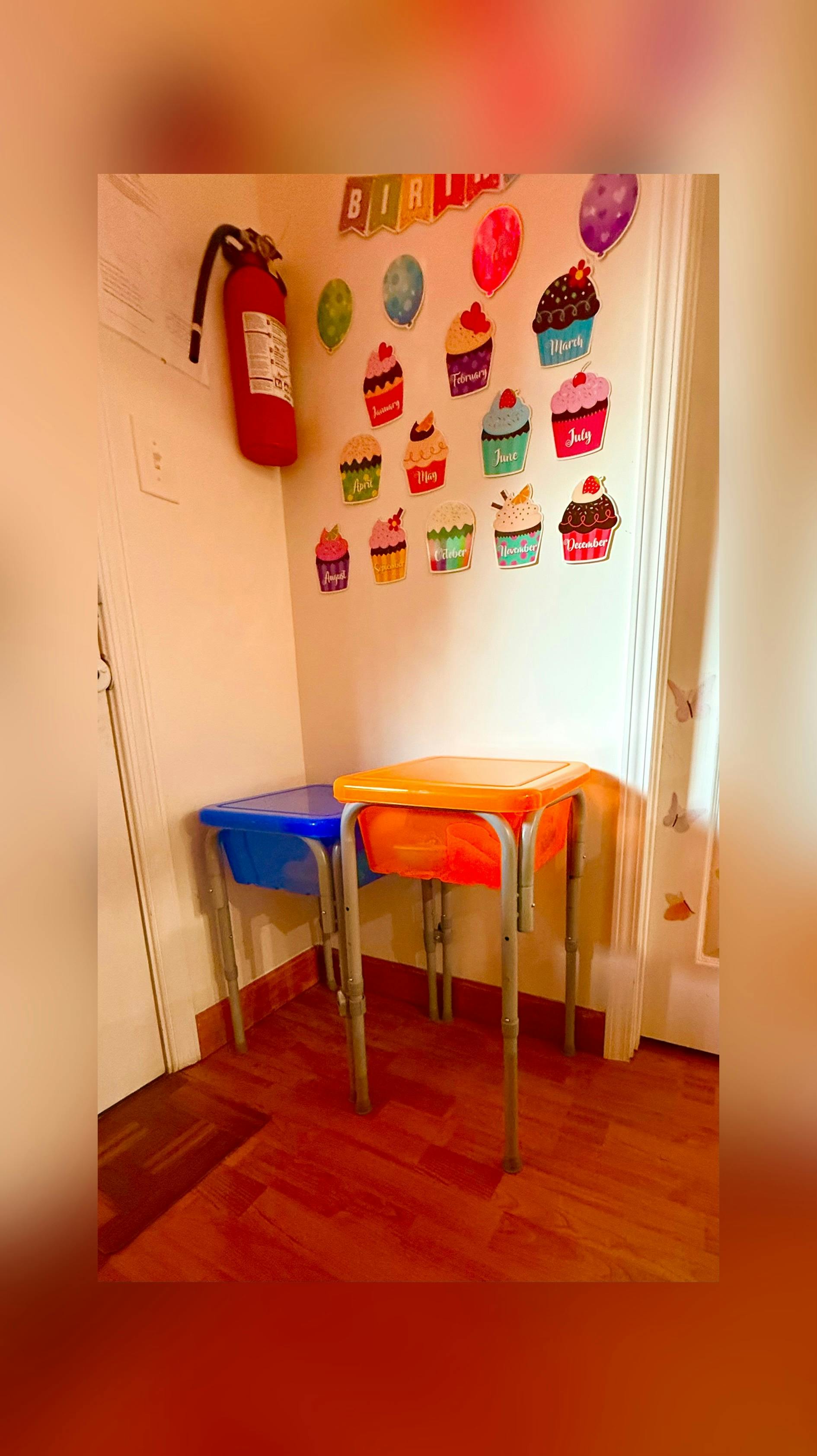 Birthday calendar with cupcake cutouts on a wall near two small plastic desks