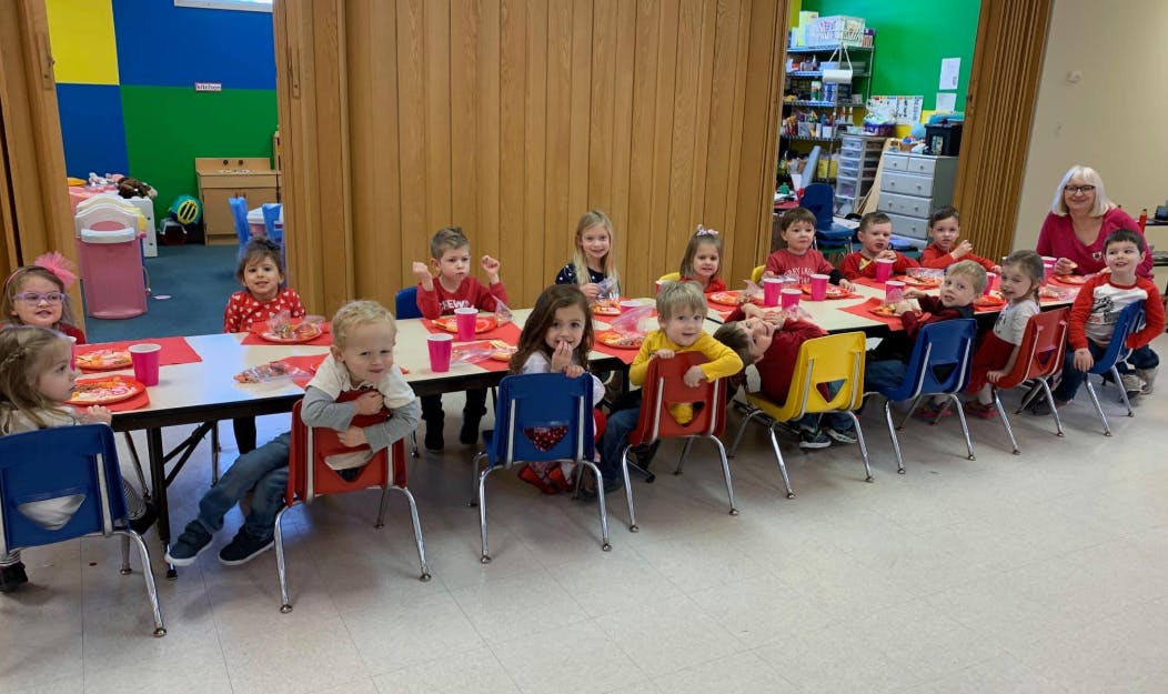 Group of children and an adult sitting at tables in a classroom