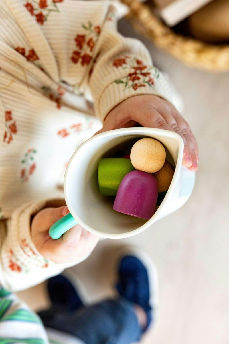 Child holding a cup filled with small wooden toy pieces