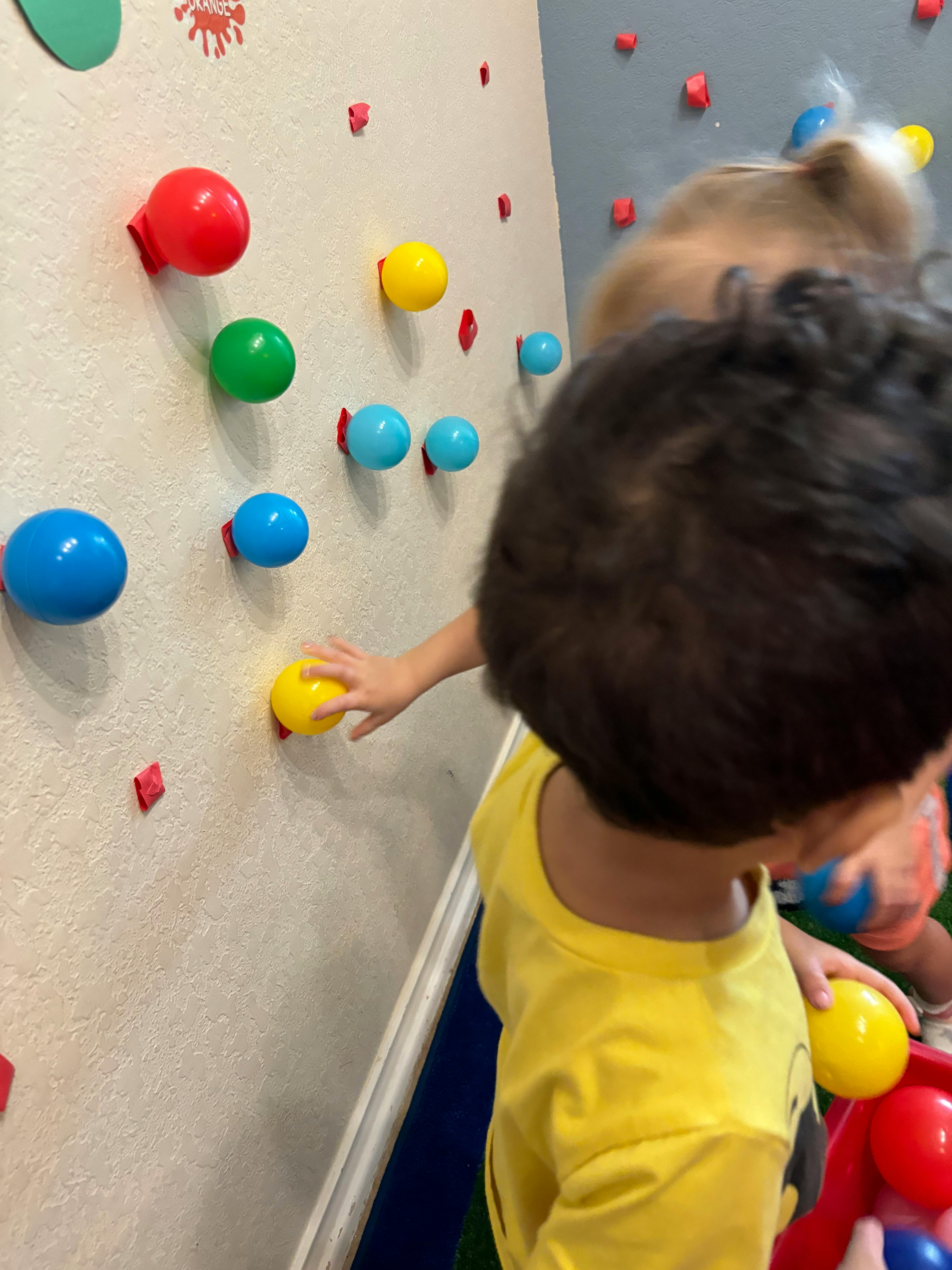 Child reaching for a yellow ball on a wall with colorful balls