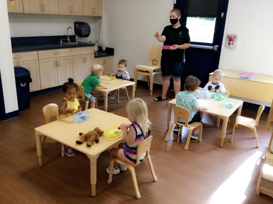 Person in mask supervising children at tables in a classroom