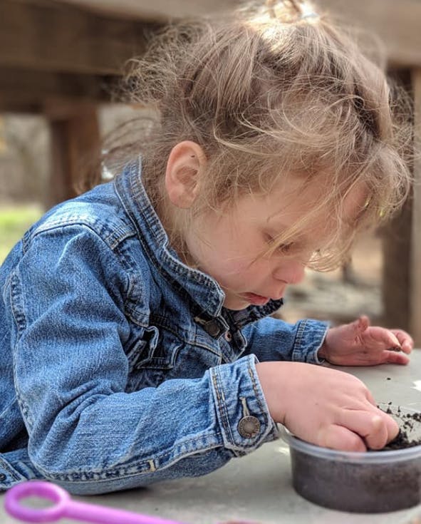 Child in denim jacket playing with dirt in a container