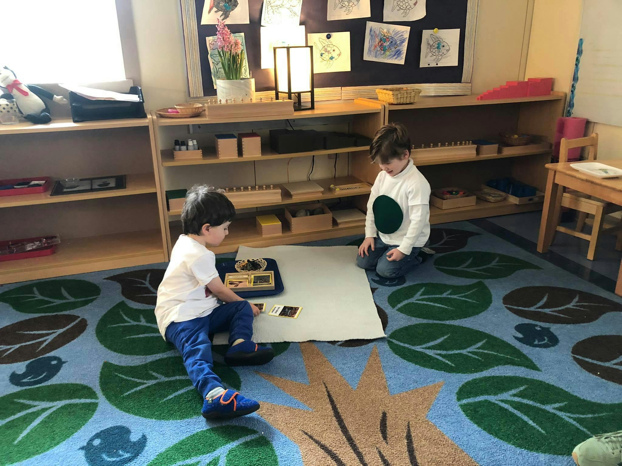 Two children playing with learning materials on a rug in a classroom