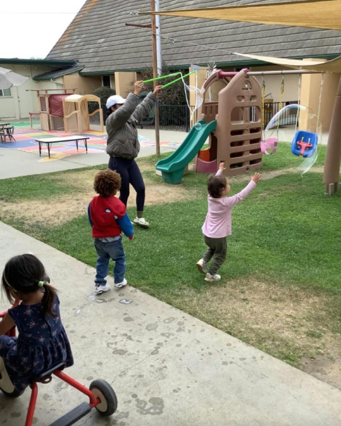 Person holding a bubble wand with children watching large bubbles outdoors