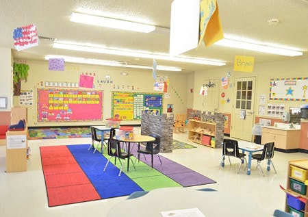 Classroom with colorful rugs, small tables, and educational displays on walls
