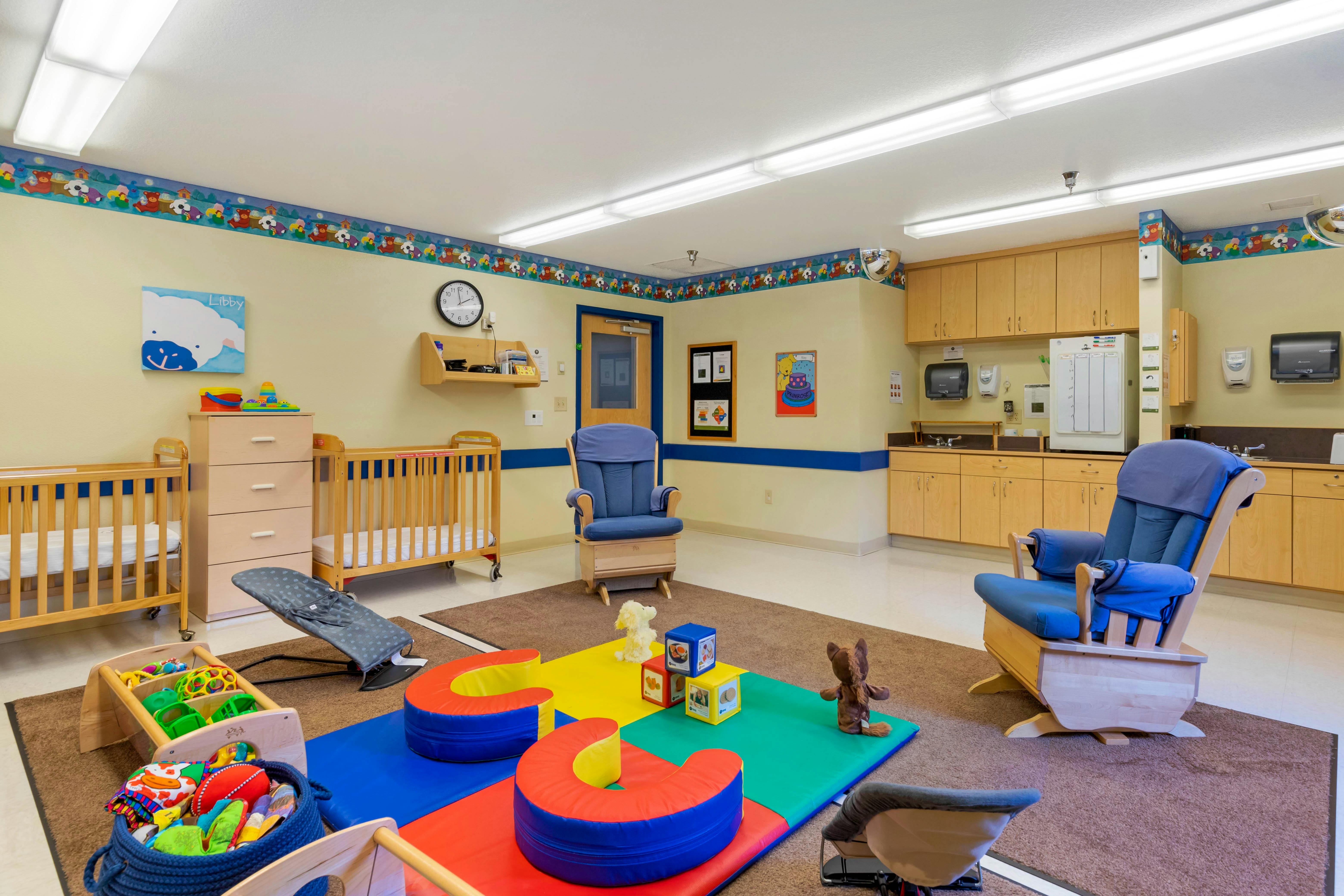 nursery room with cribs, rocking chairs, and colorful play mats on the floor