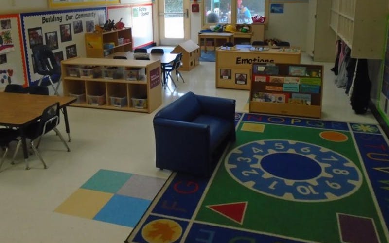 Classroom with tables, chairs, shelving units, and a colorful rug with numbers