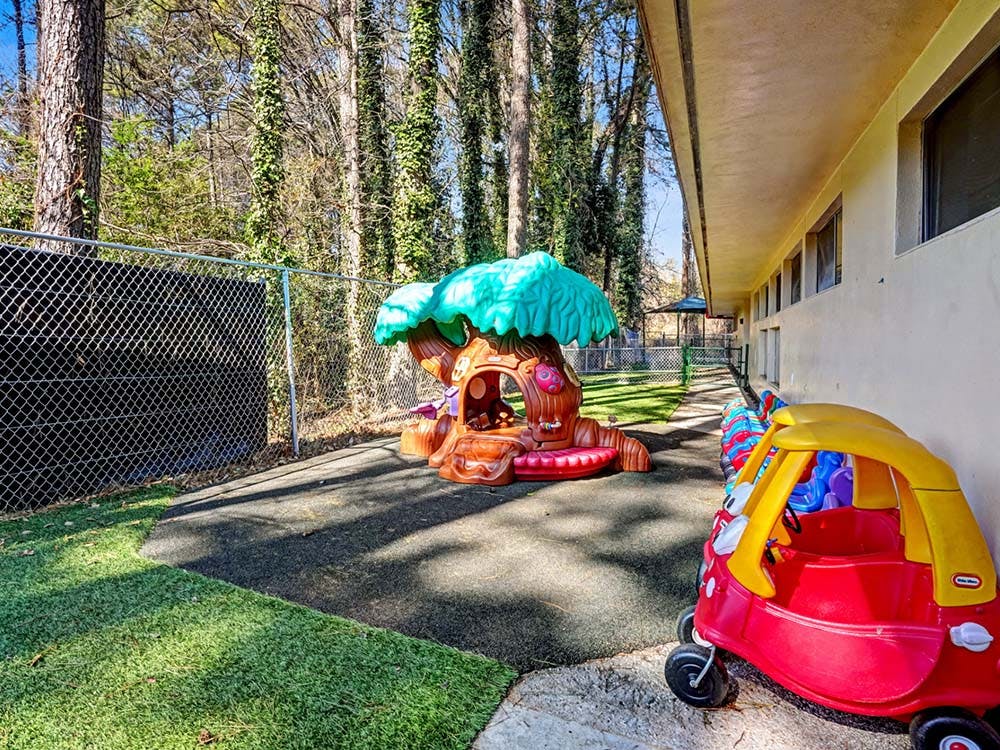 Outdoor playground with toy car and treehouse structure next to a building