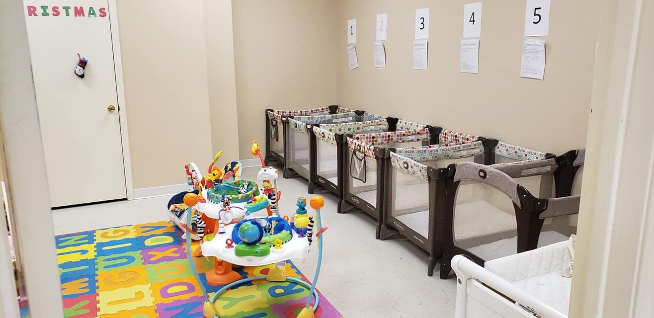 Room with multiple cribs, a play mat, and a baby activity center