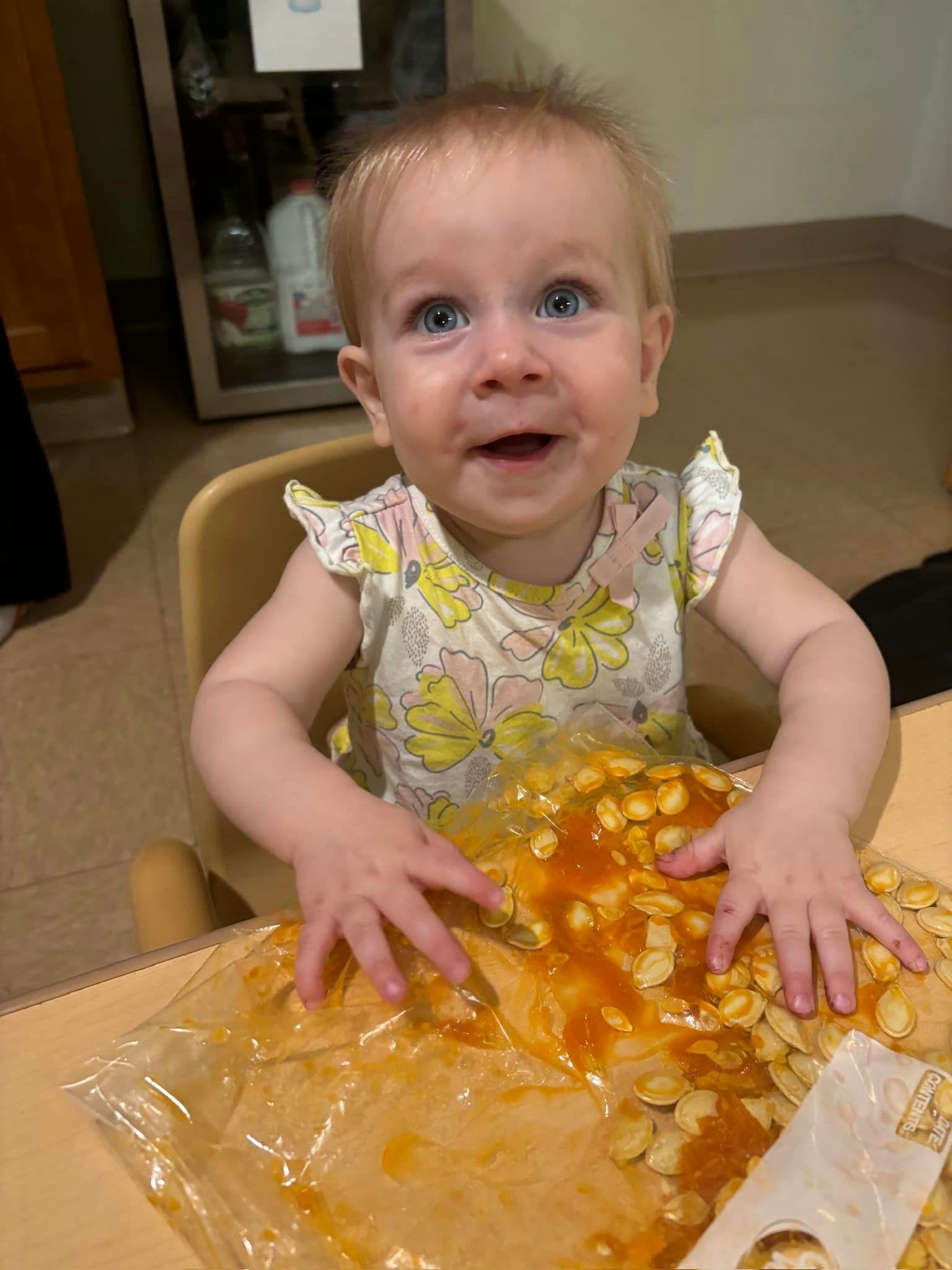 Child in a high chair playing with pumpkin guts and seeds in a plastic bag