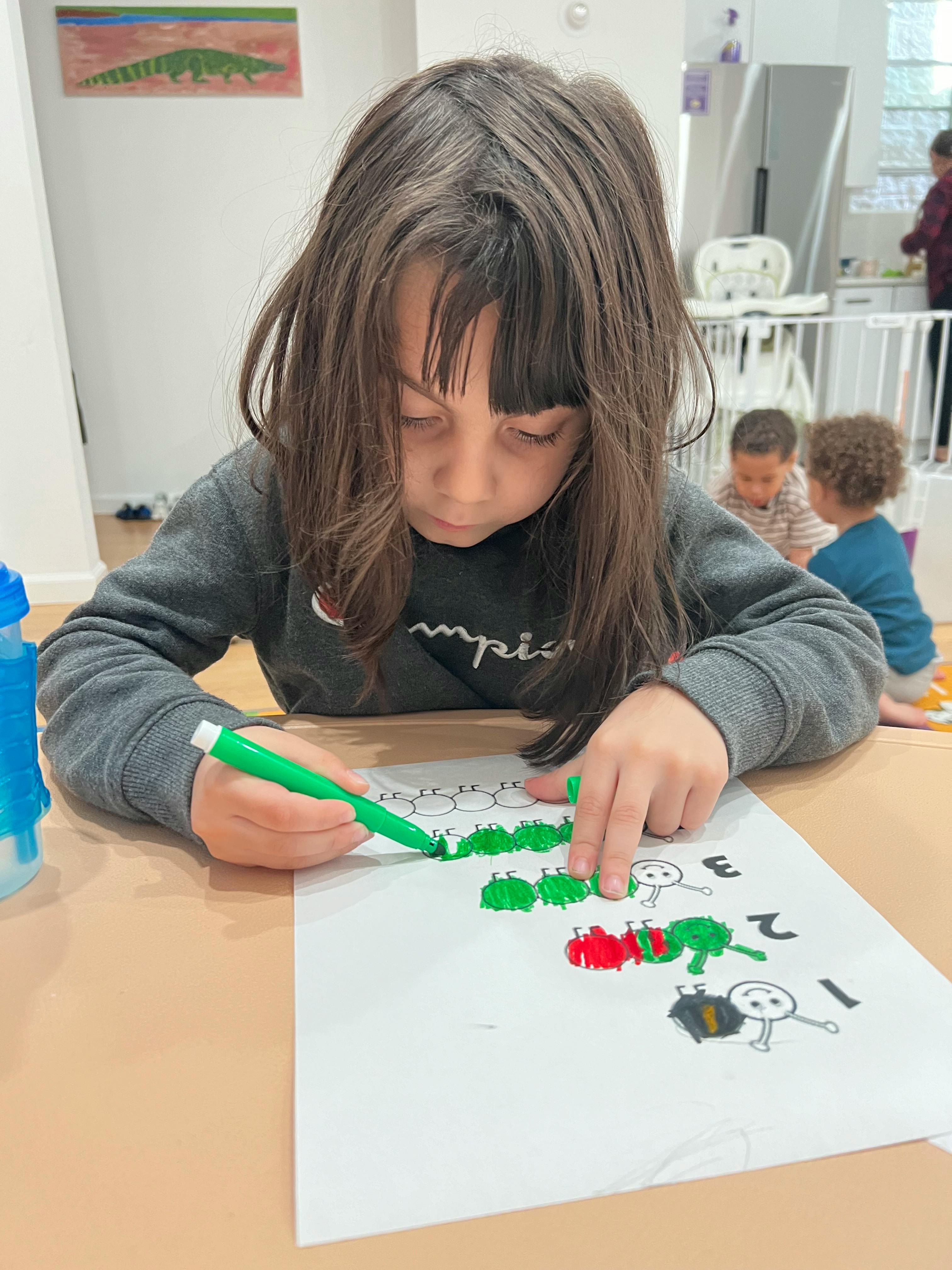 Child coloring a drawing of caterpillars on a piece of paper