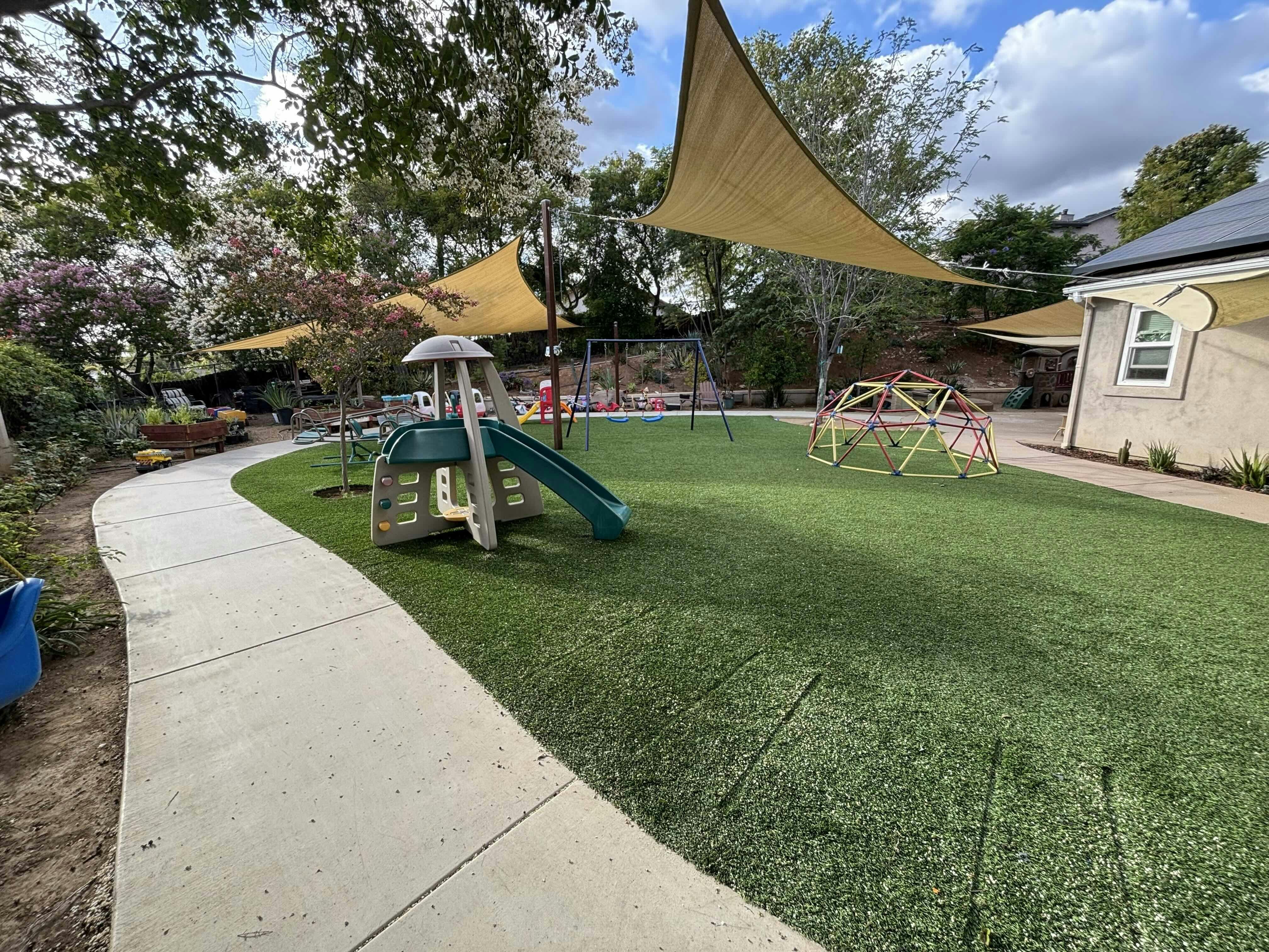 Playground with artificial turf, a green slide, colorful climbing dome, and swings