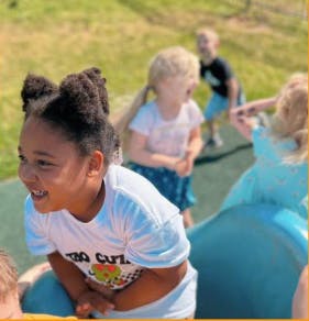 Child smiling on a slide with other children playing in the background
