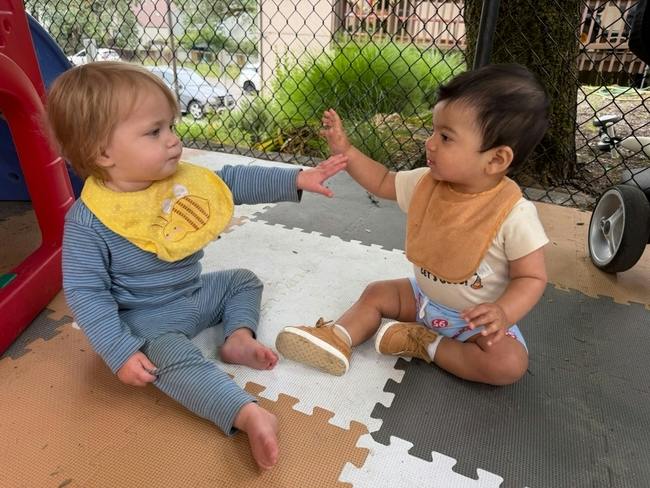 Two children sitting on a play mat reaching out to touch hands