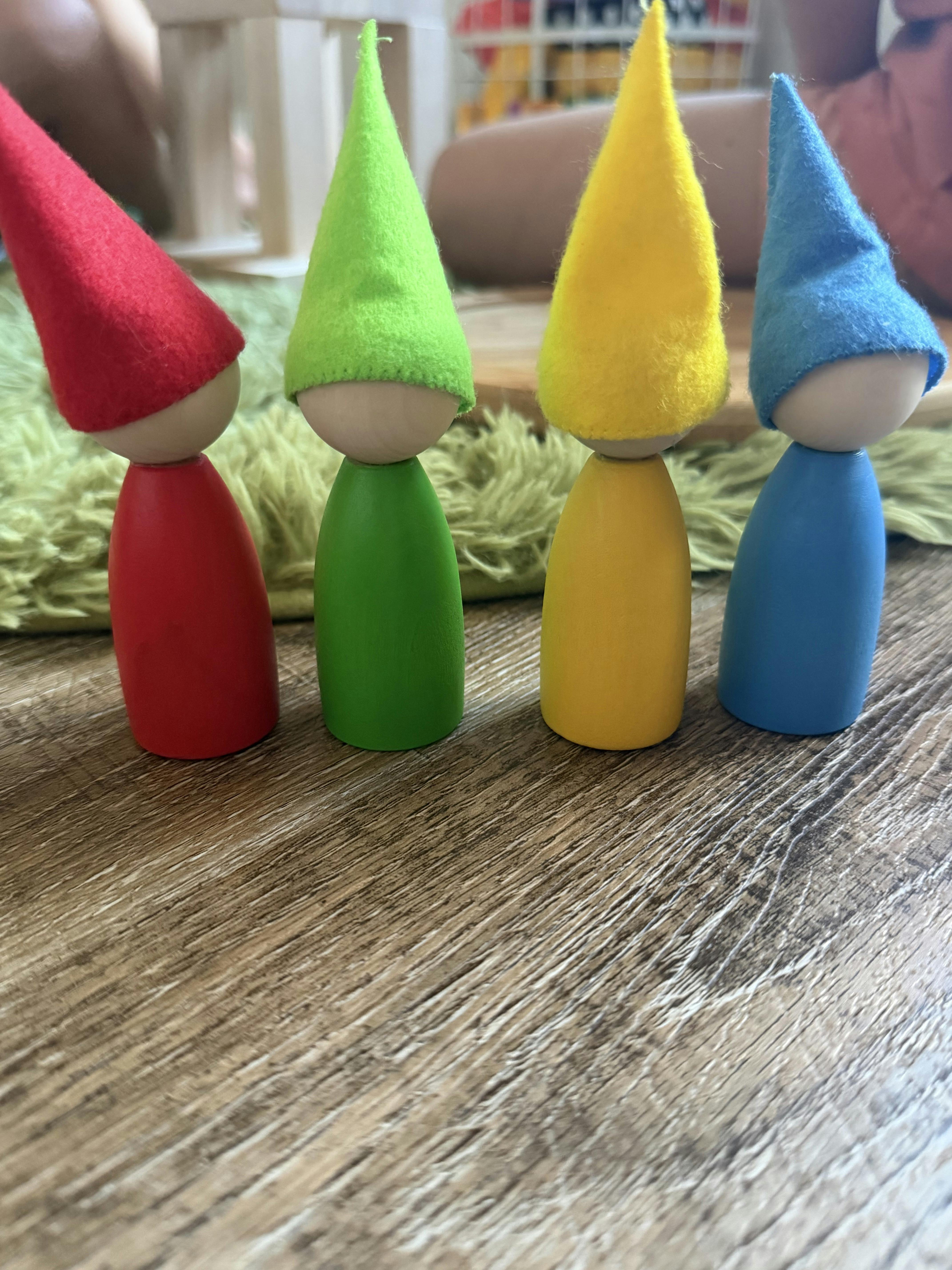 Four wooden peg dolls with colorful pointed hats on a wooden floor