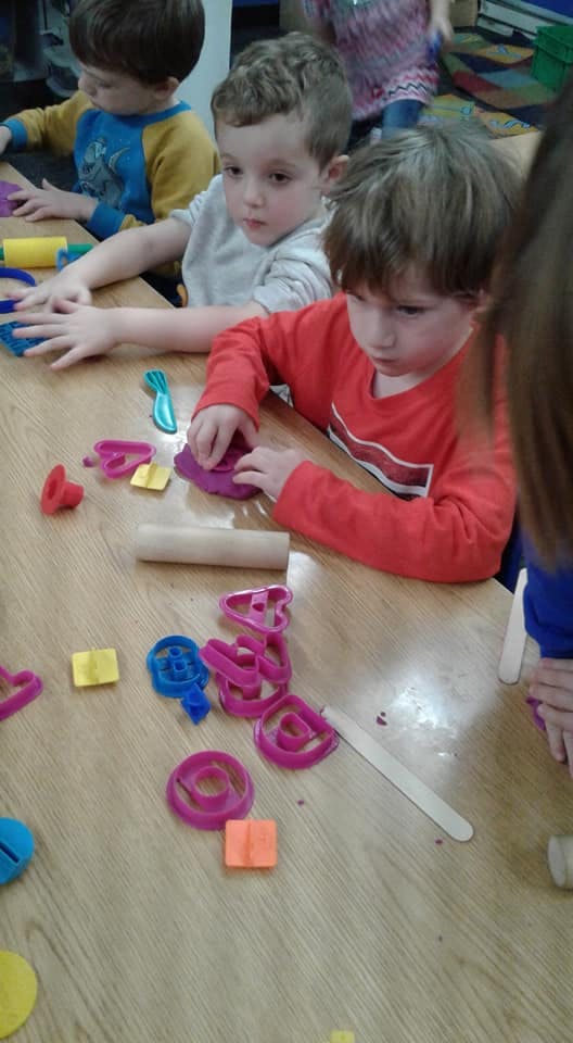 Children playing with modeling clay and cookie cutters at a table