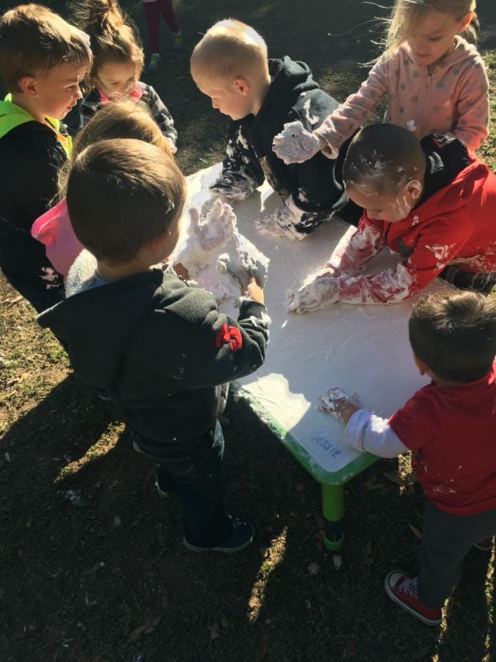 Children playing with a white substance on a table outdoors