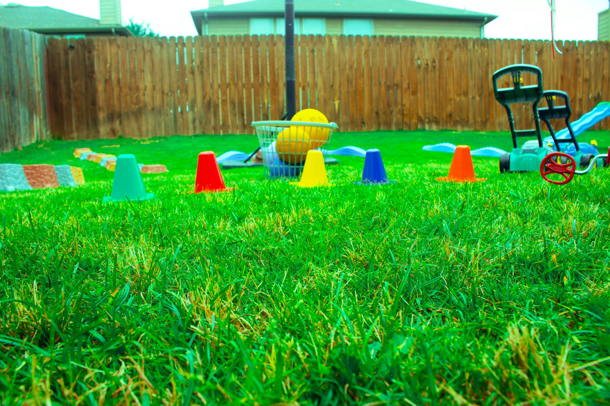 Colorful cones on a green lawn with a fence and house in the background