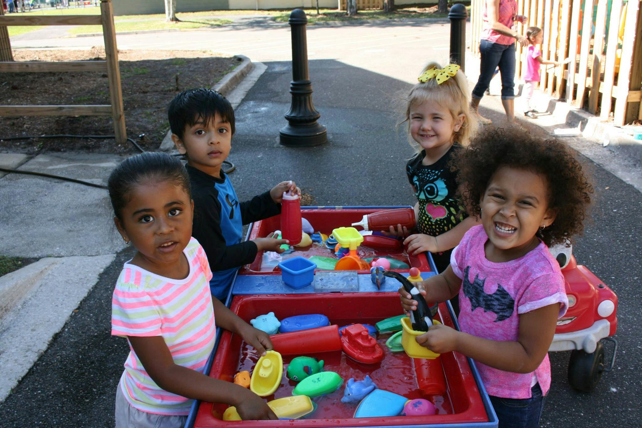 Four children playing with water and toys at a red activity table