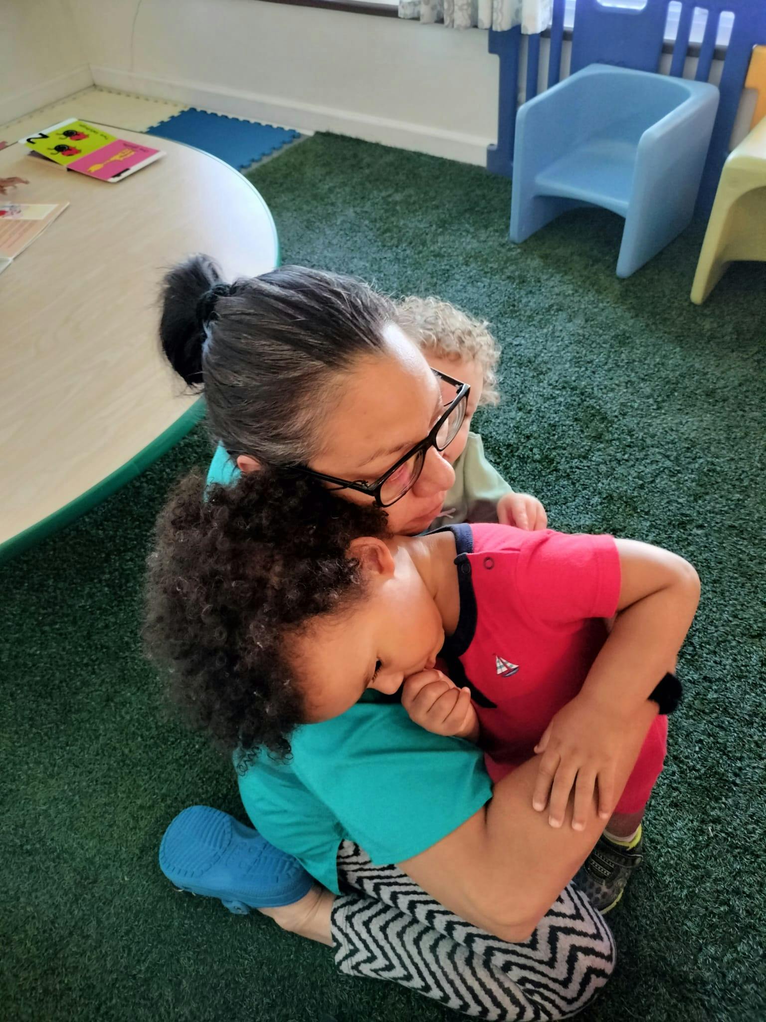 Person kneeling and hugging a child, another child behind them