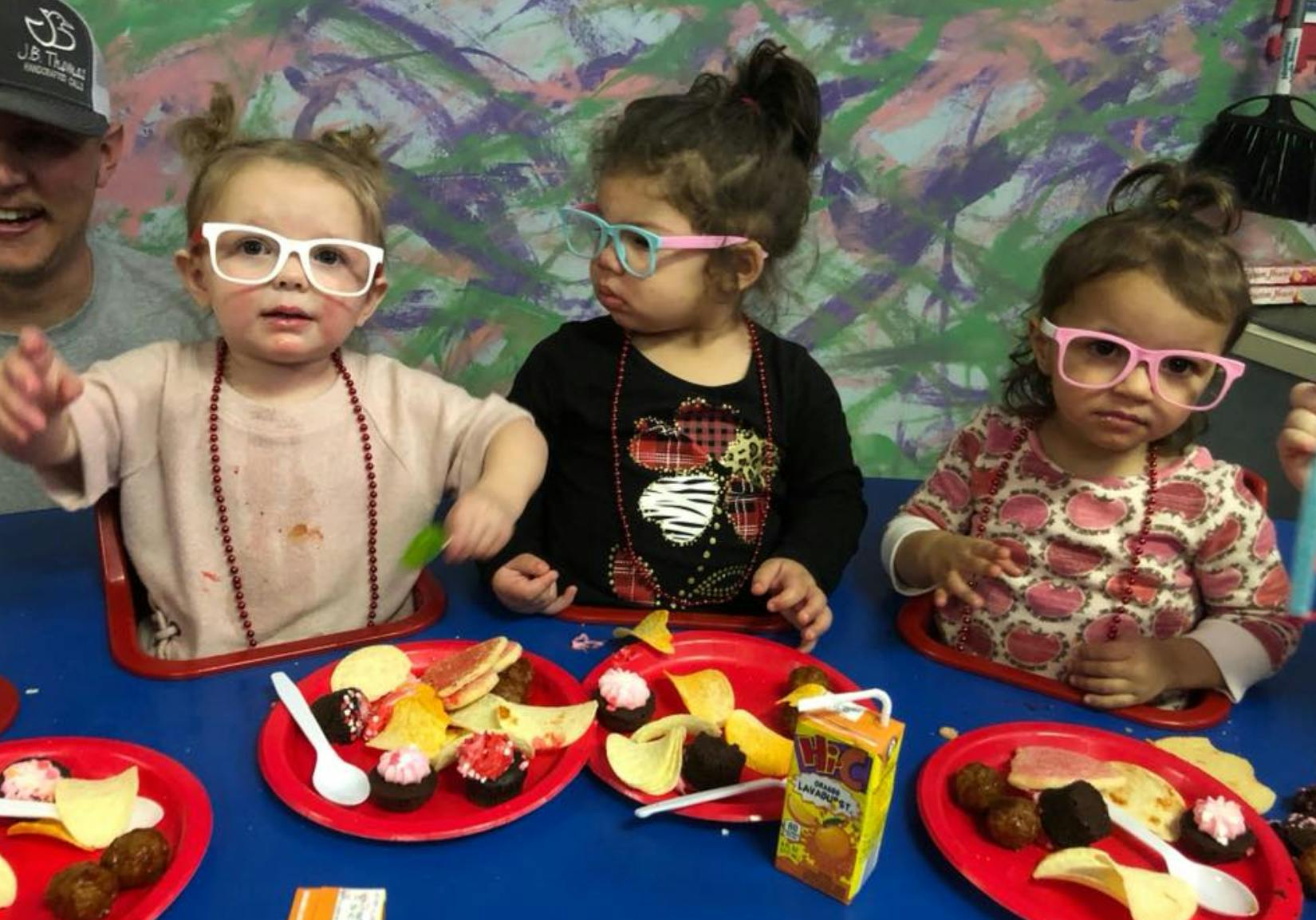 Three children wearing glasses and eating snacks at a table