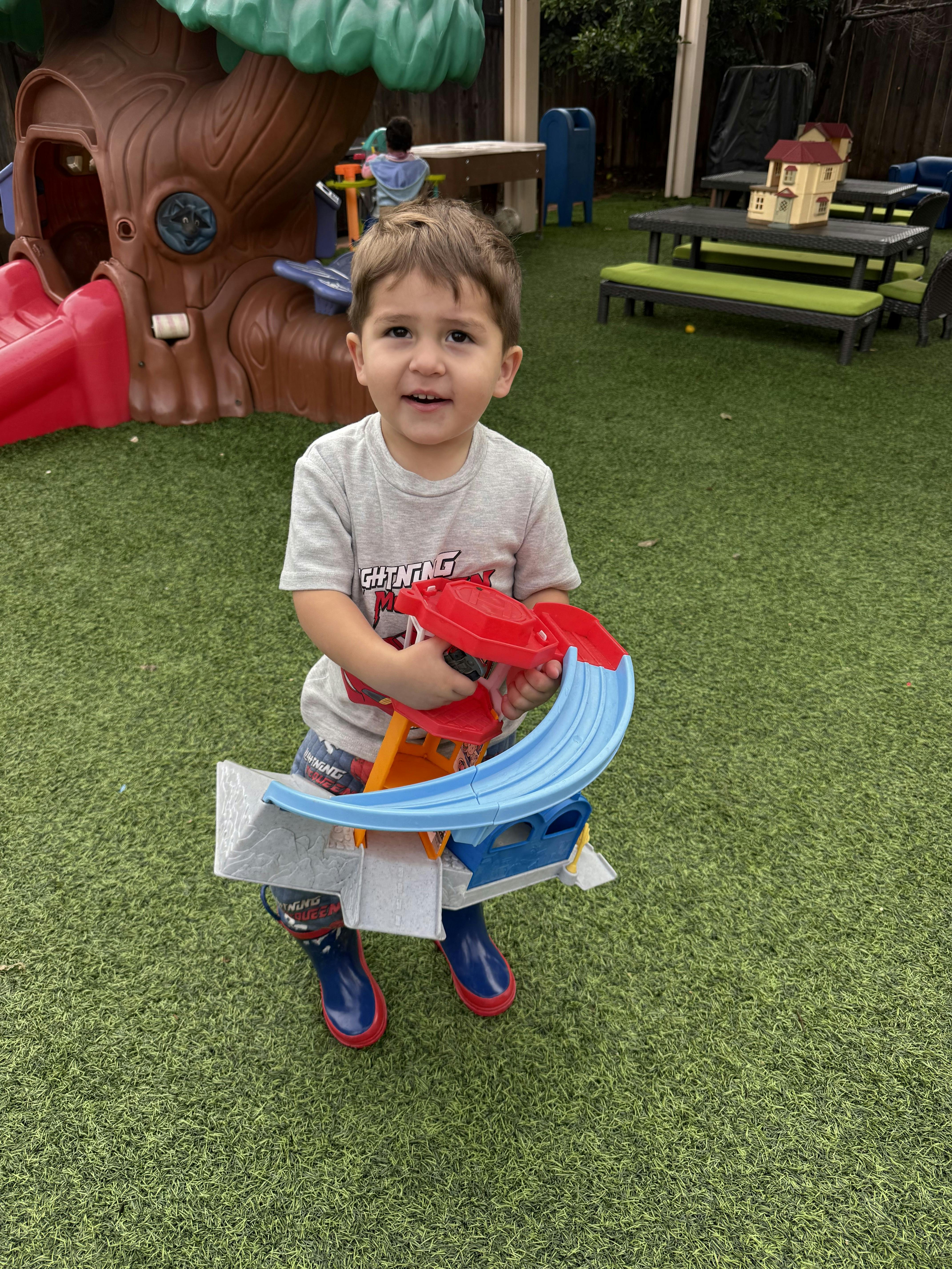 Child standing on grass holding a toy car ramp