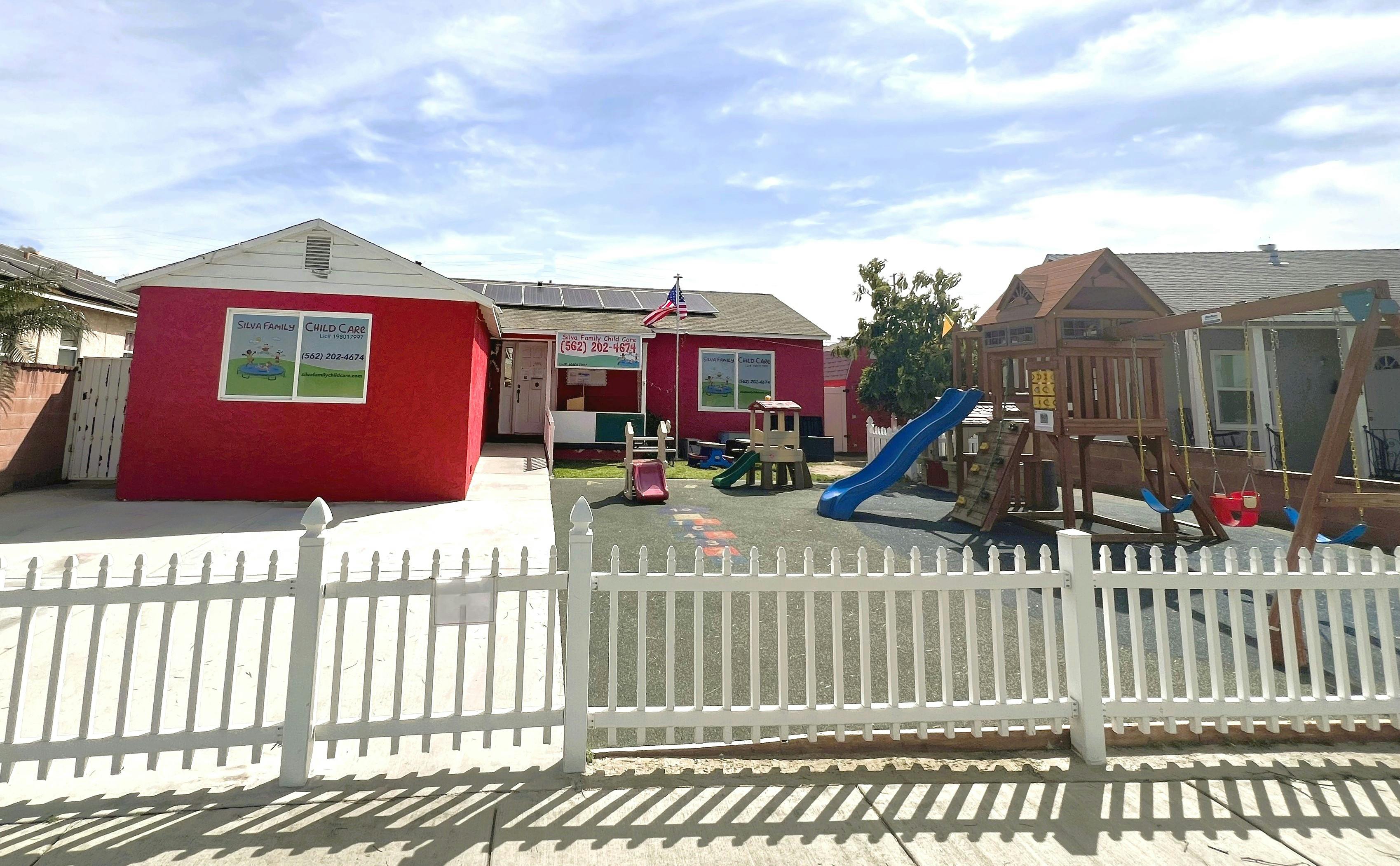 Red building with a white picket fence and playground