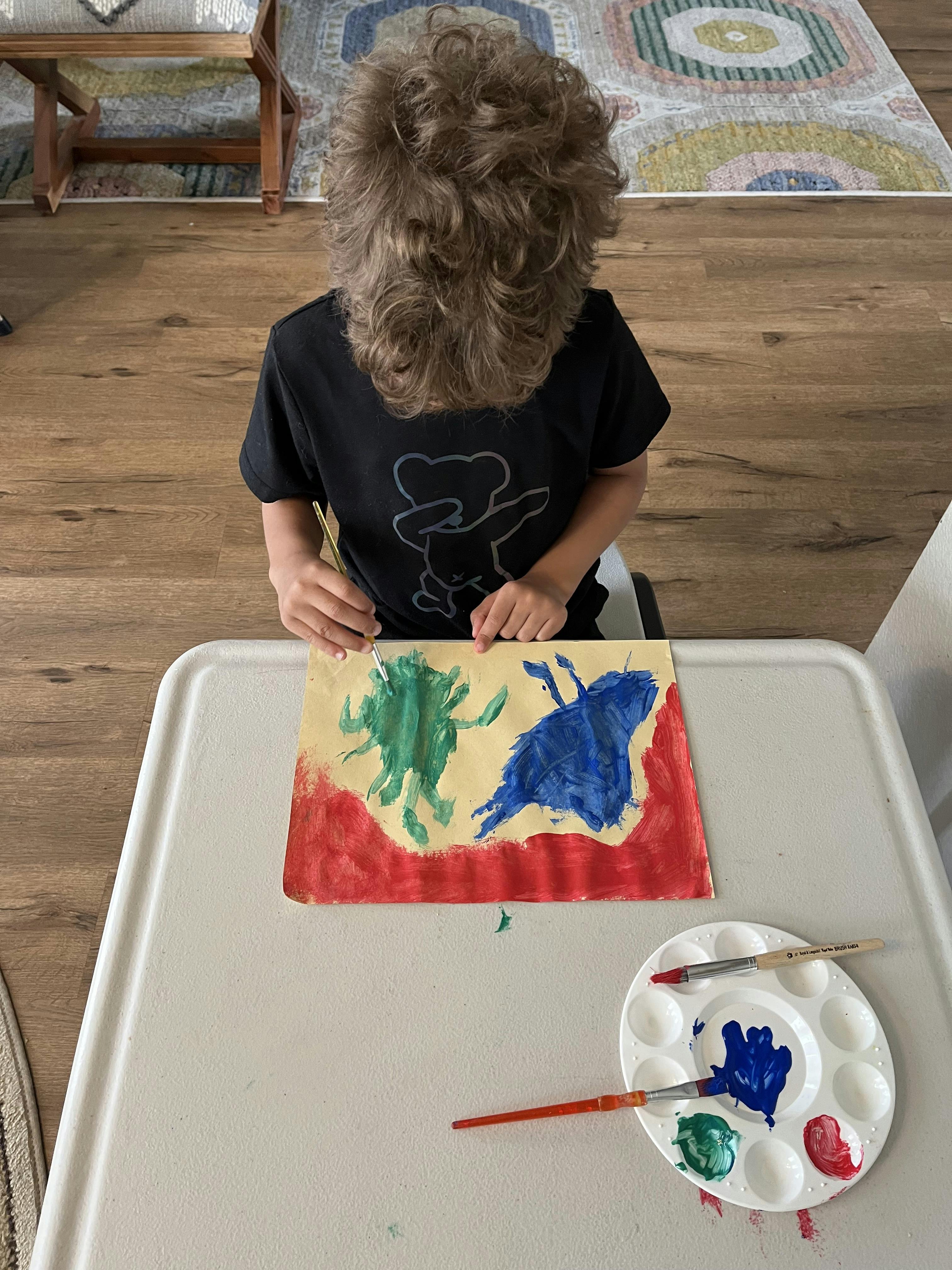 Child painting on paper with a palette and brushes on a table
