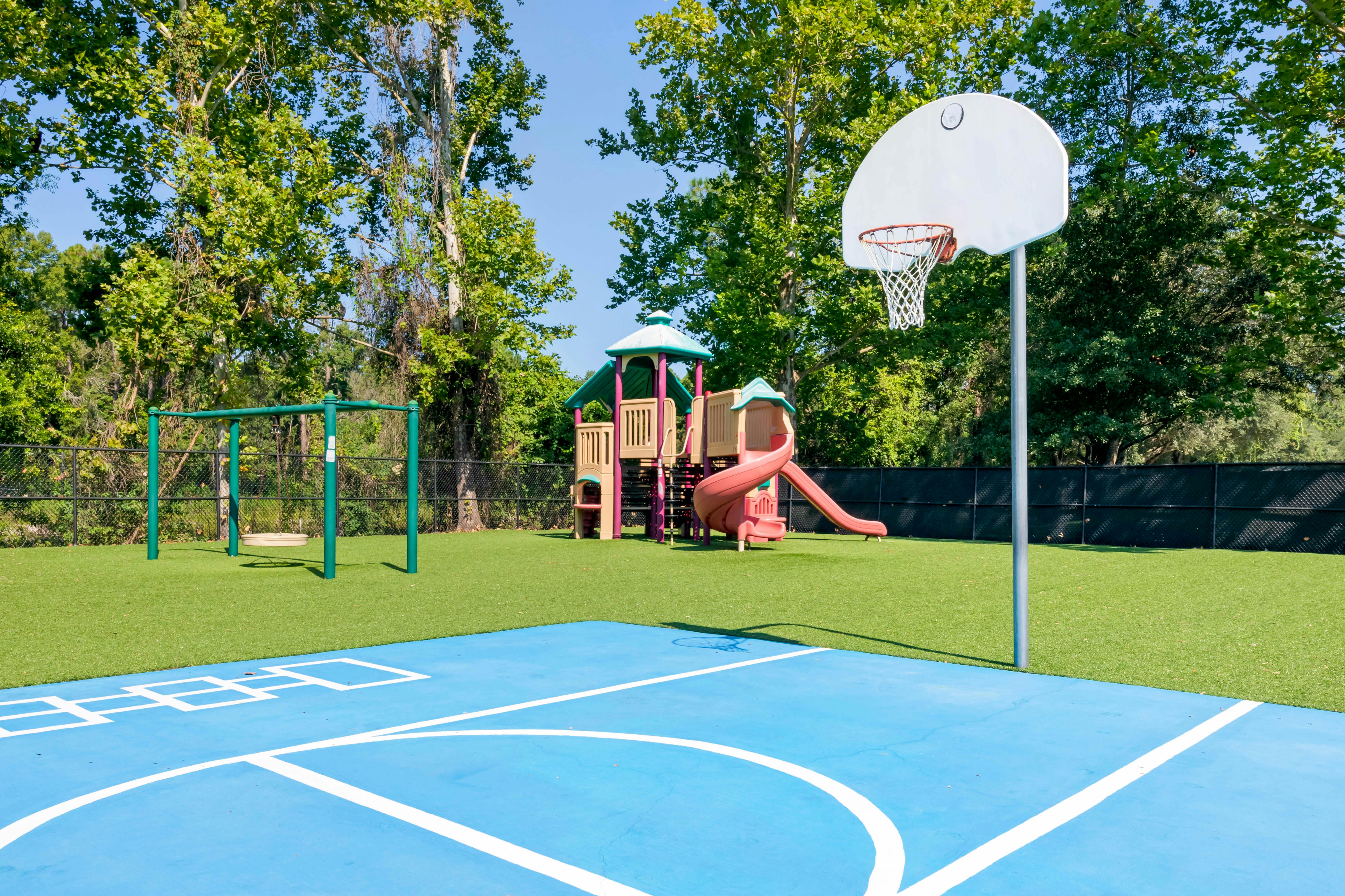 Basketball hoop on a blue court with a playground and swings in the background