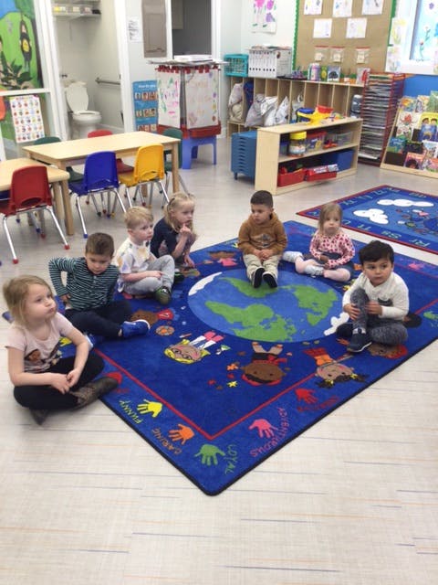 Children sitting on a blue rug with a world map design in a classroom