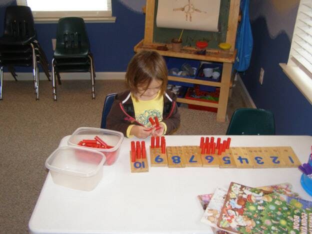 Child playing with red counting pegs and numbered blocks at a table