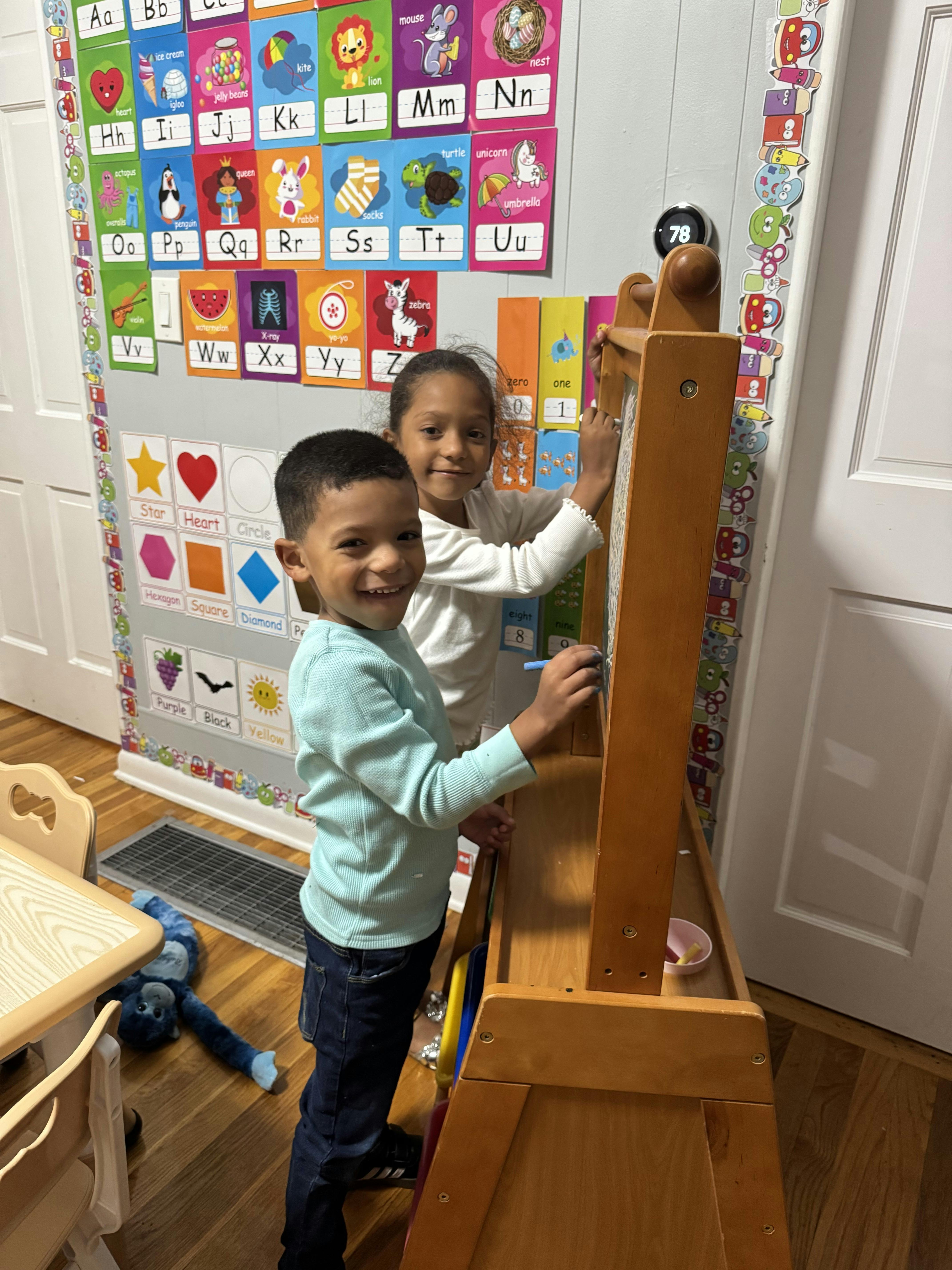 Two children drawing on an easel in a room with alphabet charts