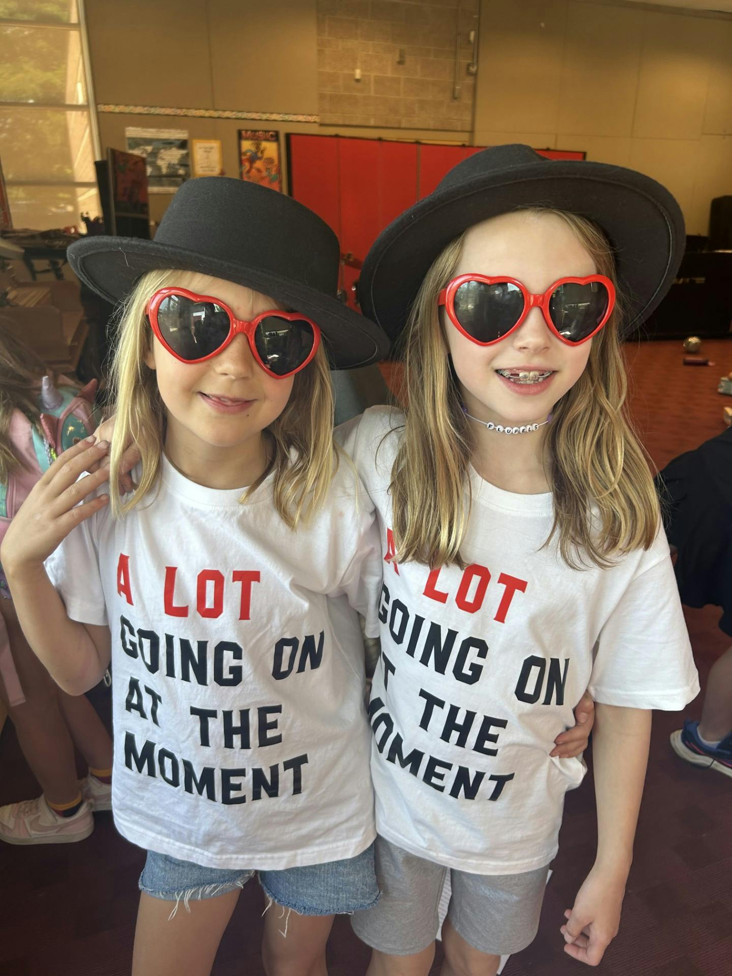 Two children wearing hats, heart-shaped sunglasses, and matching t-shirts