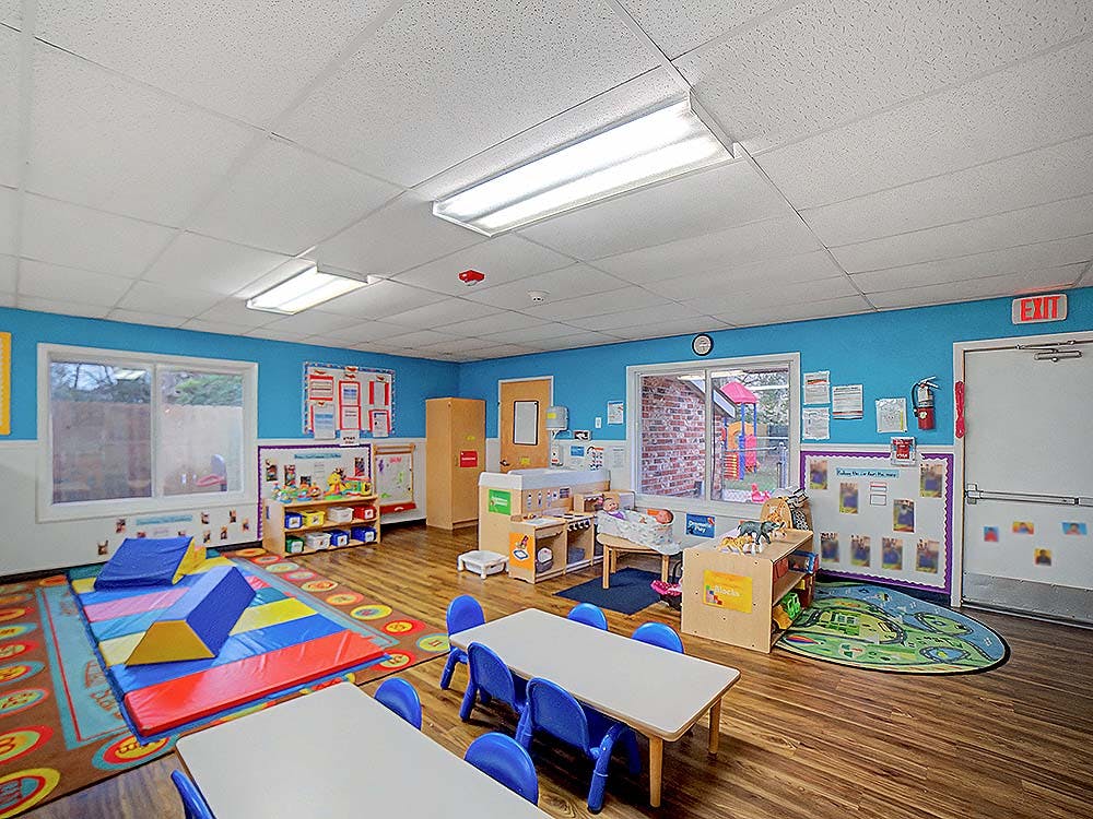 An empty classroom with activity stations, small tables, and soft play equipment
