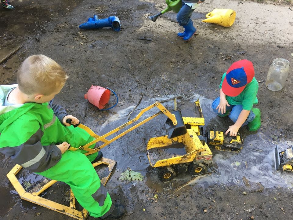 Two children playing with toy construction vehicles in dirt