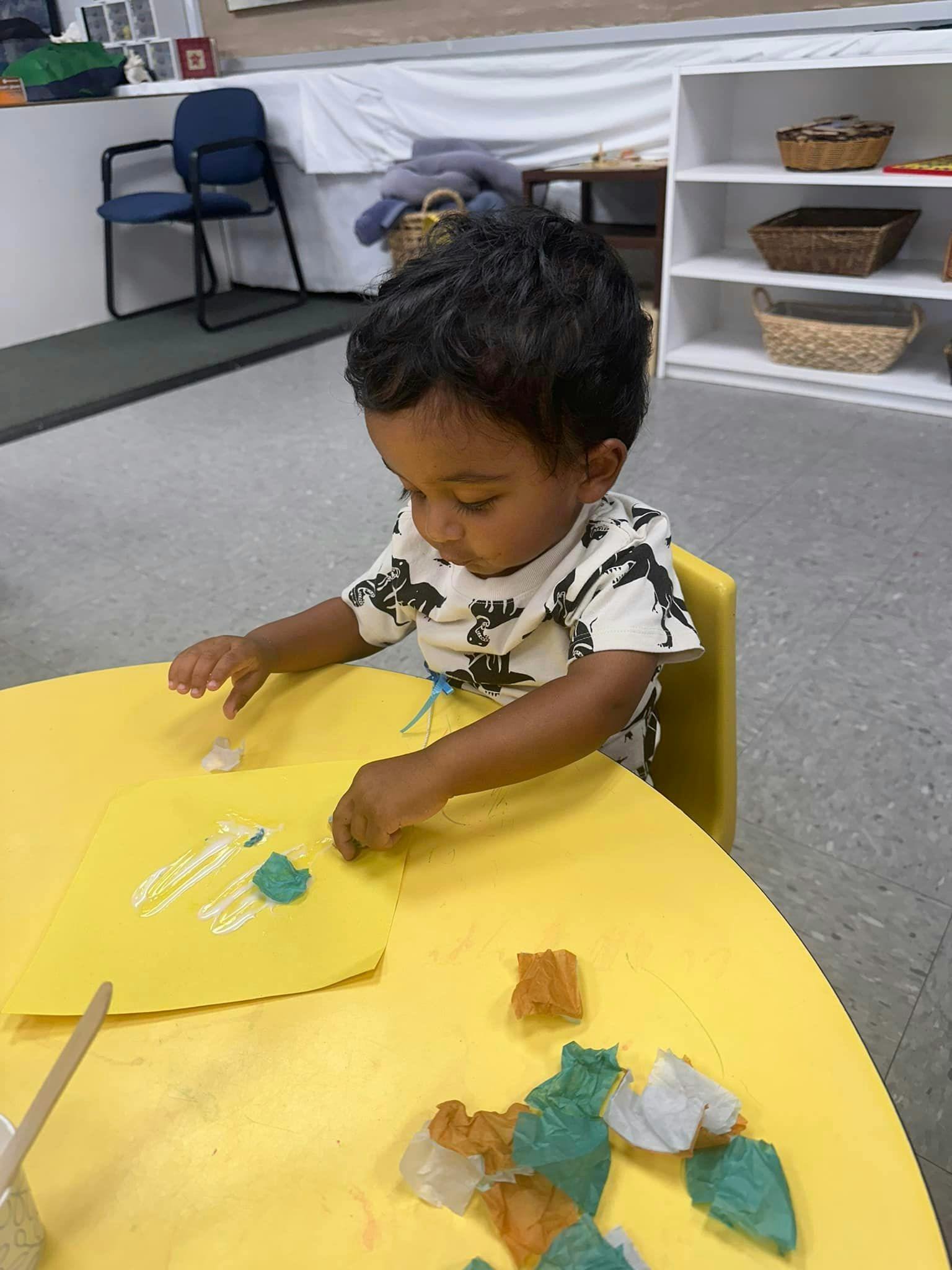 Child sitting at a yellow table doing an art project