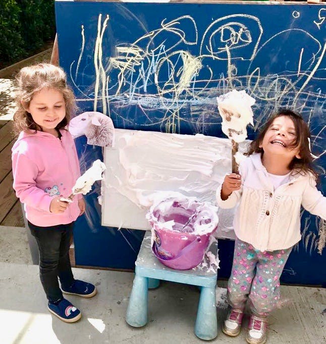 Two children painting with shaving cream on a blue board