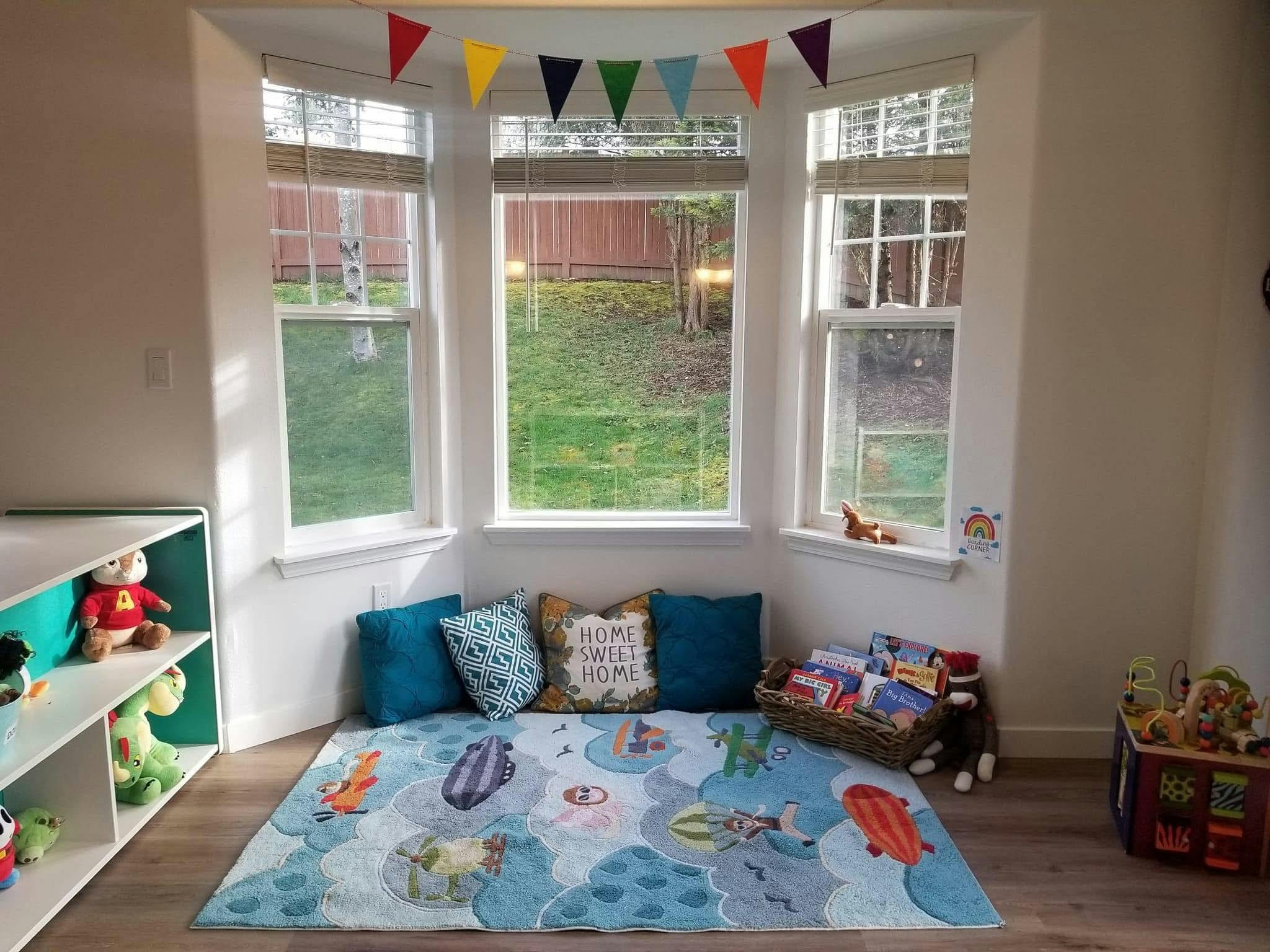 Play area with a rug, pillows, and books near a bay window