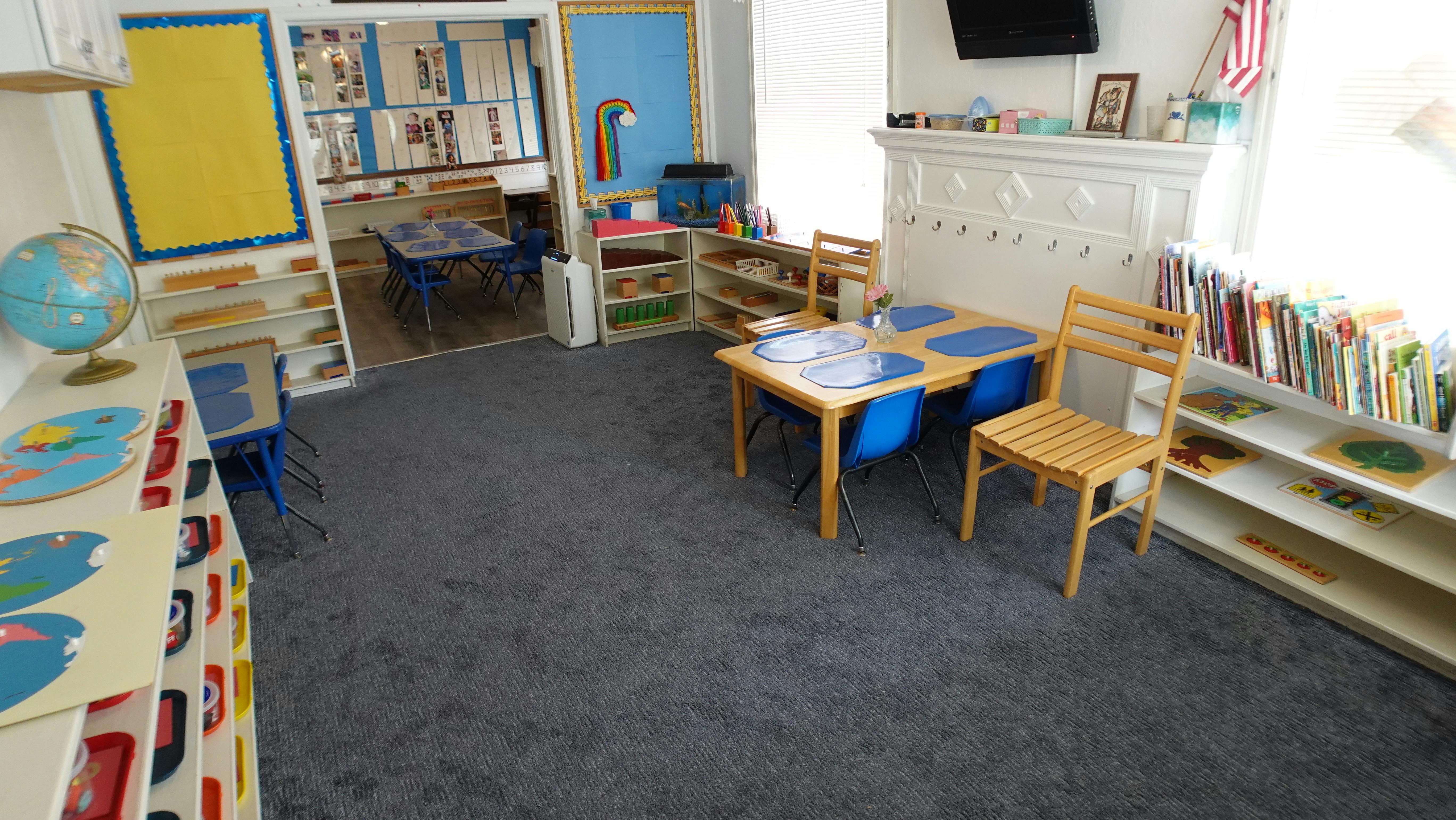Classroom with small tables and chairs, shelves with books and learning materials
