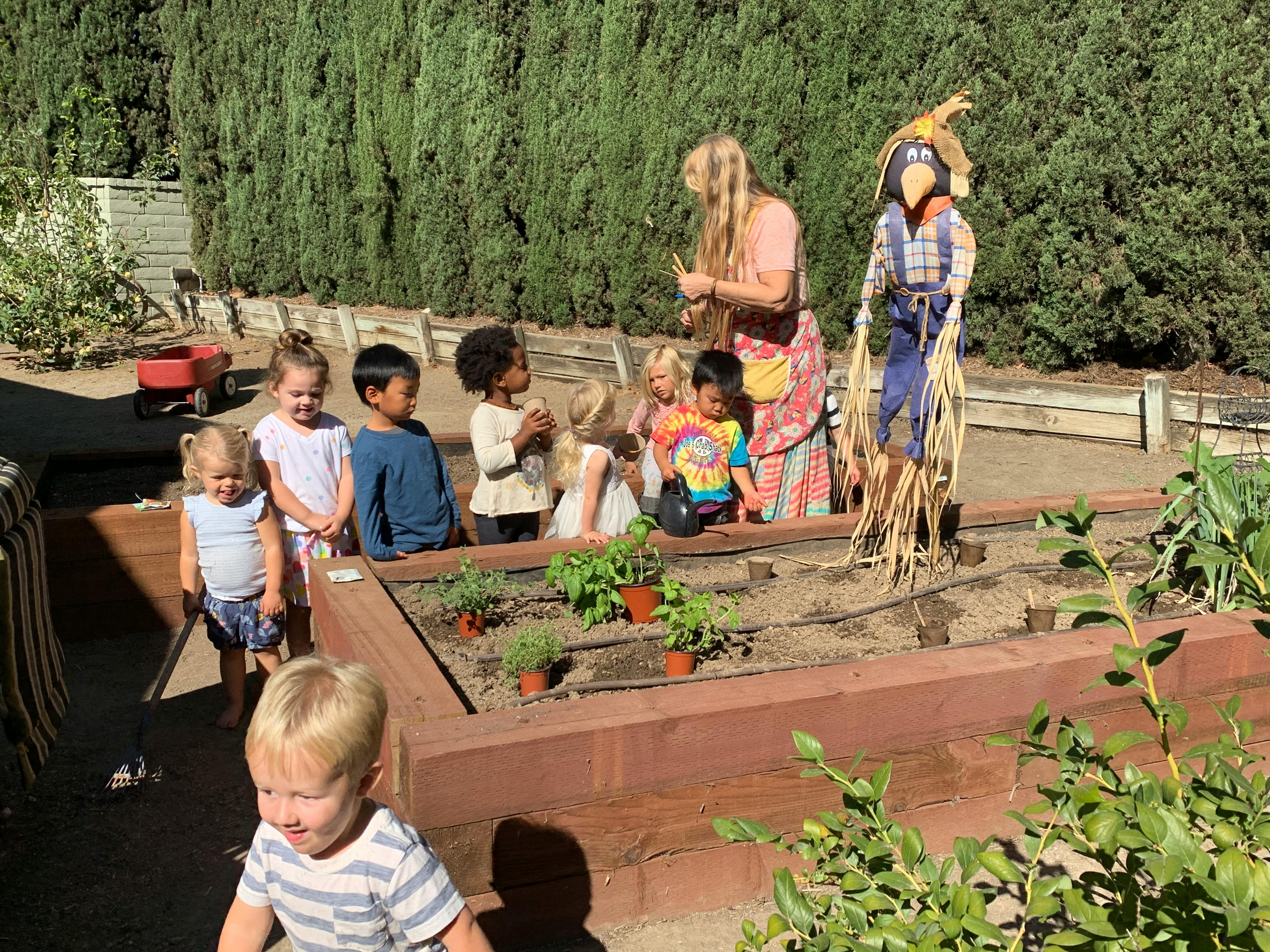 Adult and children gathered around a garden bed with a scarecrow