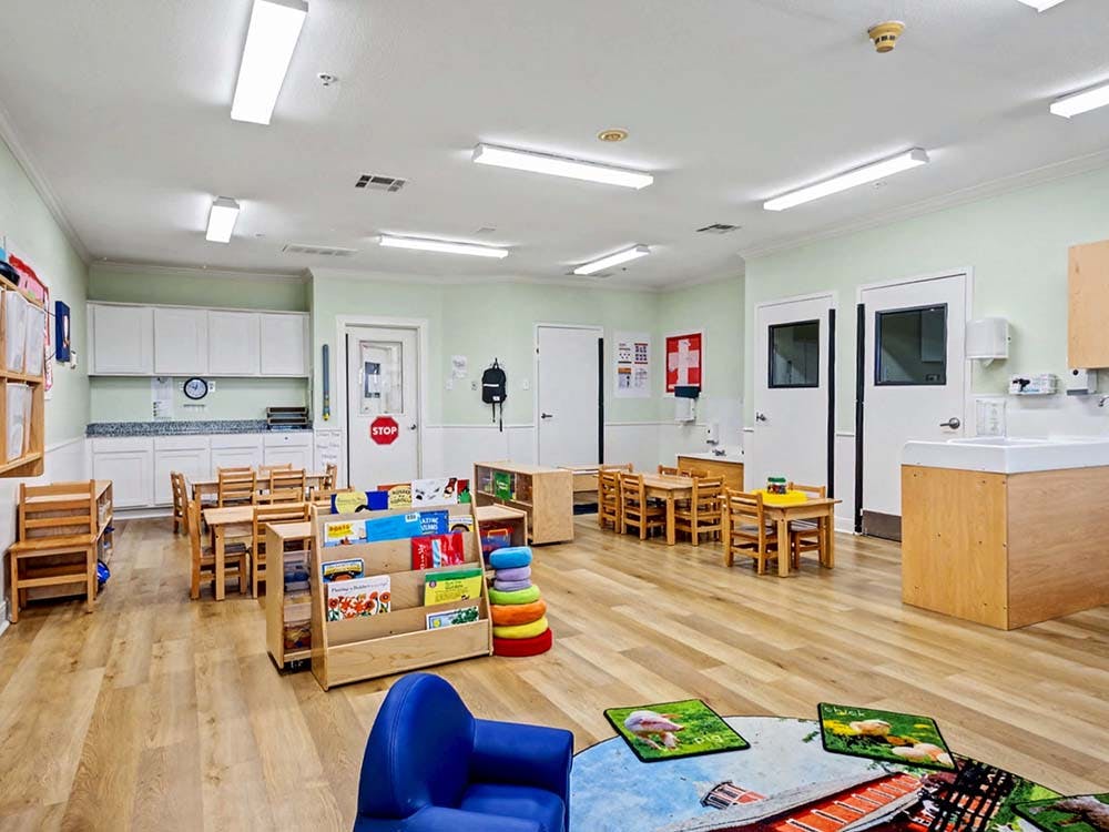Empty classroom with small tables and chairs, a bookshelf, and counters