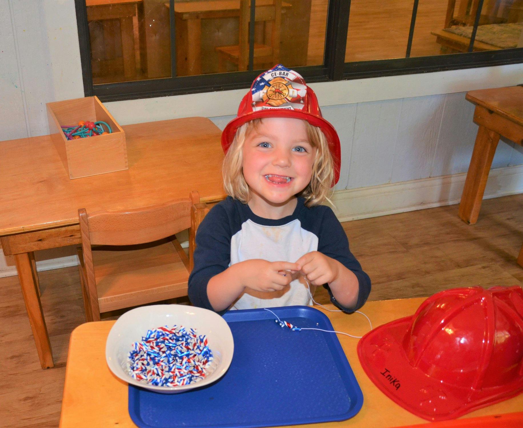 Child in a firefighter hat stringing beads at a table
