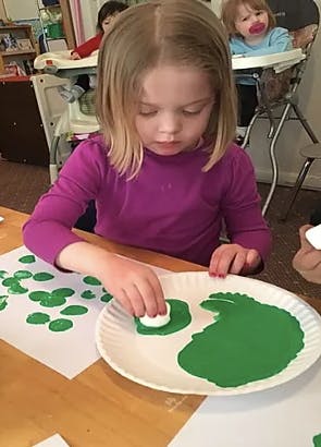 Child painting with green paint and a sponge